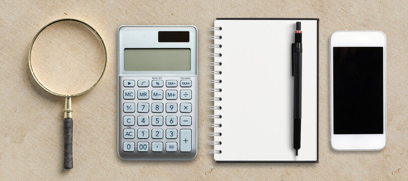 magnification glass, notepad, pen, smartphone and calculator on paper background