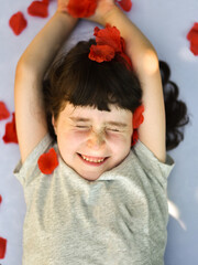 Smiling little girl squints as rose petals fall on her