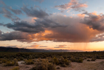 Sunset, thunderclouds, orange sky and patchy rain in the Mojave desert with I-15 freeway in the background

