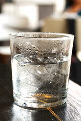 Cold ice water with ice bar in clear glass on the table and small water drop, stream at the outside of the glass from coldness.  