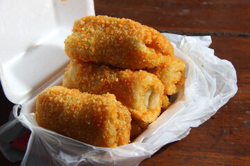 crispy roll cake with egg and sausage flavor. snacks with white and pastic containers on a wooden table