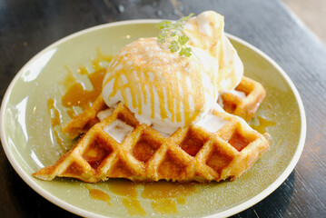 Close up, macro top-view of Cafe dessert Caramel Salty Waffle on top with whipping cream scope and small mint leave. Presented in soft and selective spot focus and blurred area.