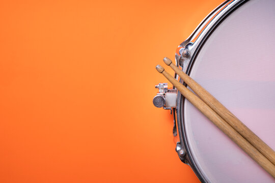 Drum stick and drum on orange table background, top view, music concept