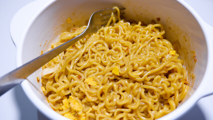A tasty instant fried noodle (Indomie Goreng) mixed with scrambled boiled egg in a white bowl. Side view of delicious fried noodle