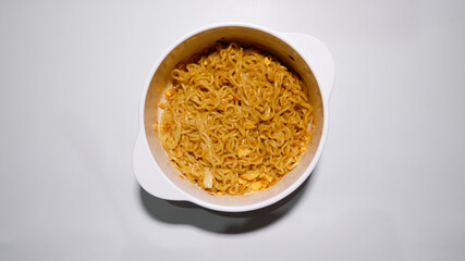 A tasty instant fried noodle (Indomie Goreng) mixed with scrambled boiled egg in a white bowl. Top view of delicious fried noodle