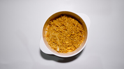 A tasty instant fried noodle (Indomie Goreng) mixed with scrambled boiled egg in a white bowl. Top view of delicious fried noodle