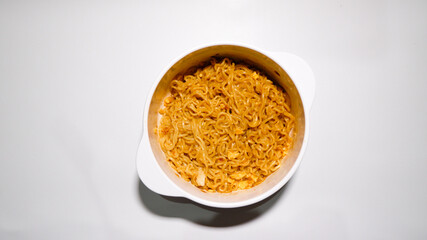 A tasty instant fried noodle (Indomie Goreng) mixed with scrambled boiled egg in a white bowl. Top view of delicious fried noodle