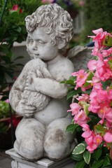 Fototapeta na wymiar Statue of a cupid, angel holding a doll in a flowered garden 2
