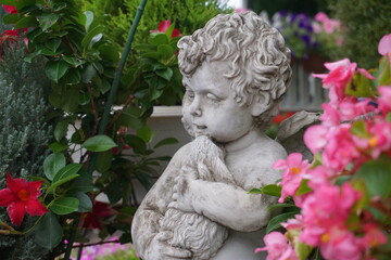 Fototapeta na wymiar Statue of a cupid, angel holding a doll in a flowered garden 3