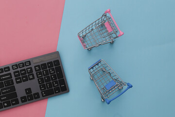 Online supermarket. PC keyboard and shopping trolley on pink blue pastel background. Top view