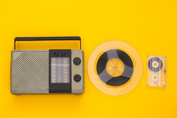 Retro poortable radio receiver and audio magnetic tape reel, audio cassette on yellow background....
