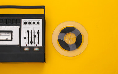 Retro flat lay. Retro stereo recorder and audio magnetic tape reel on yellow background. Top view. 80s