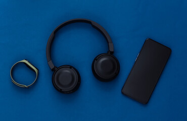 Modern gadgets. Smartphone with black stereo headphones and a smart bracelet on classic blue background. Top view