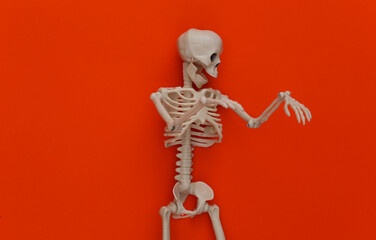 Fake skeleton on orange background. Halloween decoration, scary theme. Flat lay. Minimalism