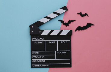 Horror movie, halloween theme. Movie clapperboard and flying decorative bats on pink blue pastel...