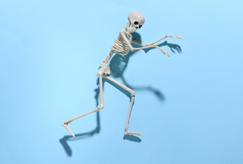 The skeleton is sneaking against a bright blue background. Halloween concept