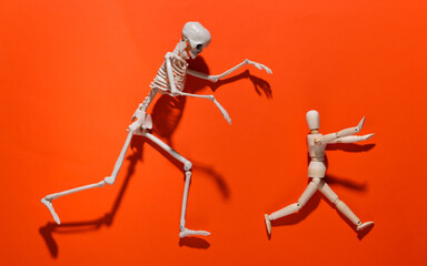 Halloween scary concept. Wooden puppet runs away from the skeleton on orange bright background