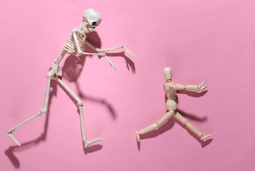 Halloween scary concept. Wooden puppet runs away from the skeleton on pink bright background