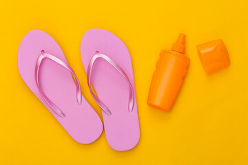 Beach vacation. Sunblock bottle and flip flops on a yellow background. Top view. Flat lay