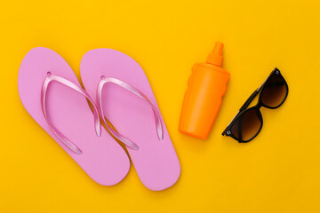 Beach vacation. Sunblock bottle, sunglasses and flip flops on yellow background. Top view. Flat lay