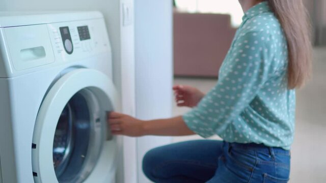 Woman loads shirts into a washer machine at home. Laundry day