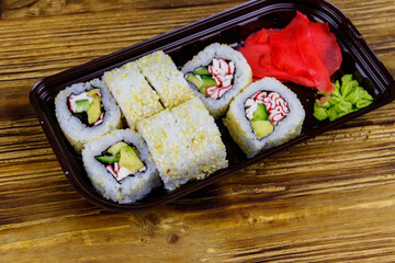 Uramaki sushi rolls with surimi in plastic box on wooden table. Top view. Sushi for take away or delivery of sushi in plastic container
