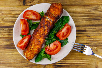 Grilled salmon fillet with spinach and tomatoes on wooden table. Top view