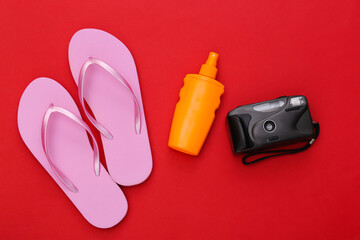 Beach vacation. Sunblock bottle, sunglasses and flip flops on red background. Top view. Flat lay