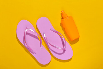 Beach vacation. Sunblock bottle and flip flops on yellow bright sunny background. Top view. Flat lay