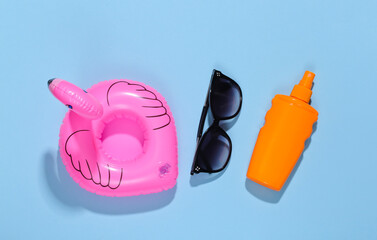 Beach vacation. Inflatable flamingo and sunblock bottle, sunglasses on bright blue background. Top view. Minimalism