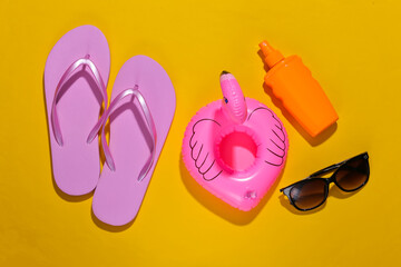 Beach vacation. Inflatable flamingo, flip flops, sunblock bottle and sunglasses on bright yellow background. Top view. Minimalism