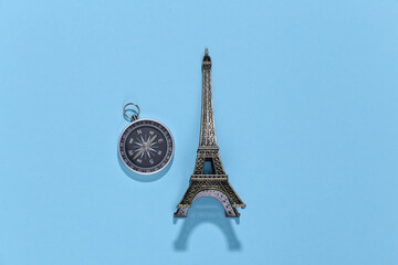 Compass and eiffel tower figurine on blue bright background. Travel, adventure flat lay. Top view