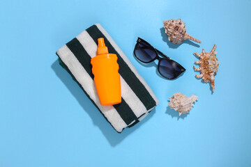 Beach vacation. Towel, sunglasses, seashell and sunblock bottle on bright blue background. Top view. Minimalism