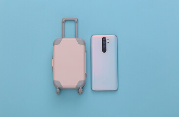 Mini toy travel luggage and smartphone on blue background. Top view