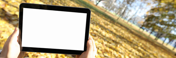 Obraz premium Focus on device reflecting mans face. Gadget shown in autumn season outdoors. Ads of device with shiny screen and copy space on it. Background of nature and leaves