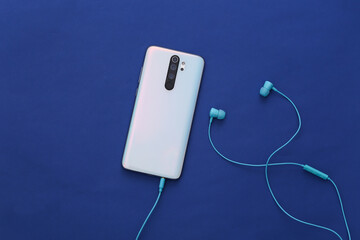 Smartphone and earphones on classic blue background.