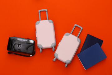 Two toy travel luggage and passport, camera on orange background. Travel planning. Top view. Flat lay
