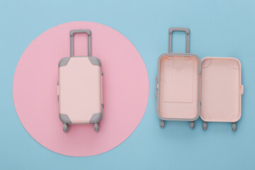 Travel planning. Two toy travel luggage on blue background with pink circle. Top view. Flat lay