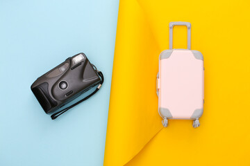 Travel planning. Toy travel luggage and camera on yellow blue paper background. Top view. Flat lay