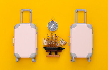 Travel planning. Toy travel luggage, ship and compass on yellow paper background. Top view. Flat lay
