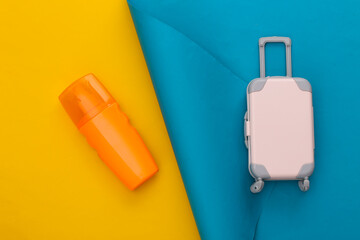 Travel planning. Toy travel luggage and sunblock bottle on blue yellow background. Top view. Flat lay