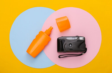 Sunblock bottle and camera on colored background. Top view