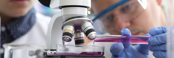 Man pours liquid into test tube under microscope. Production methods drugs are constantly being...