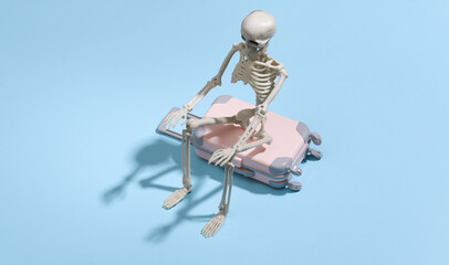 Toy skeleton with travel luggage suitcase on blue background. Travel concept