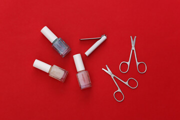 Manicure scissors, nail polish bottle and clippers on red background. Beauty concept. Nail care. Top view