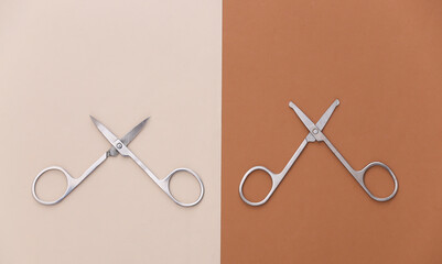 Two pairs of nail scissors on a beige-brown background. Top view