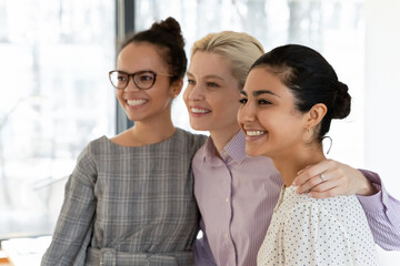 Happy diverse millennial female colleagues friends hug posing for group picture in office together, smiling multiracial young women coworkers embrace at workplace, show unity and friendship at work