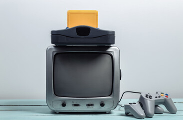Old tv receiver with retro game console, joysticks on a white wall background. Retro gaming. 80s