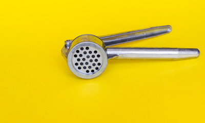 a steel hand press for chopping garlic lies on a bright contrasting yellow background. High quality photo