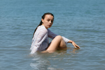 hot summer girl in a light shirt sits marine in the water
